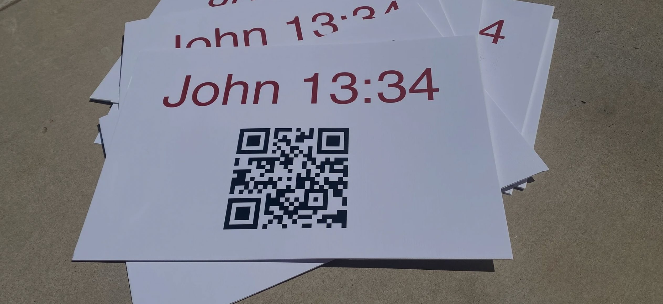 Printed John 13:34 signs with a QR code, ready to hold and share.